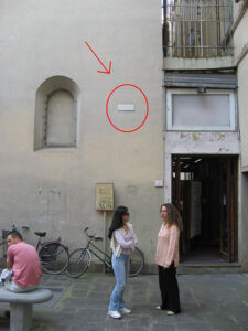 Two women standing before wall in Florence with a white high water mark of the 1966 flood. At this point the marker is about 4 metres (13 ft) high. The aftereffects of this flood gave birth to #AskAConservator day.
