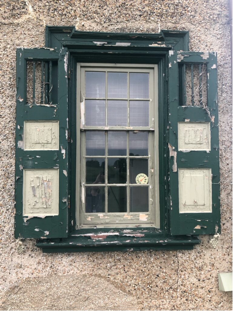 Gatehouse window before shutter conservation project. Peeling green and white paint.