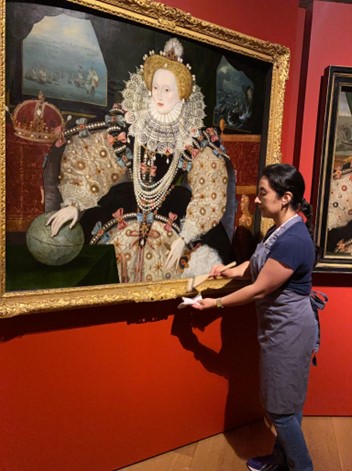 Maria Bastidas Spence cleaning the frame of a painting of Elizabeth II of England